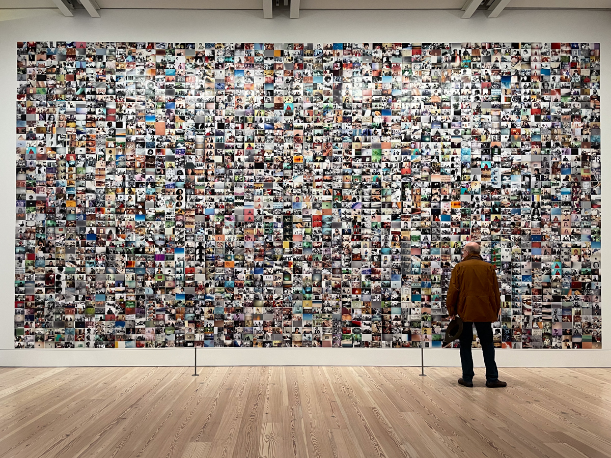 An end-to-end view of Carmen Winant's "The Last Safe Abortion", installed at The Whitney Museum. A man is standing in front of the several thousand images, mainly of women on the phone, doing office work.